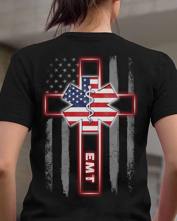 Black EMT t-shirt with white cross and American flag, symbolizing dedication and patriotism.