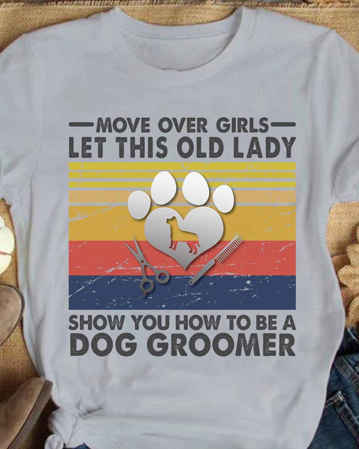 White t-shirt for dog groomers with a playful graphic of a dog, scissors, comb, and heart. Bold quote states 'Move over girls, let this old lady show you how to be a dog groomer'.