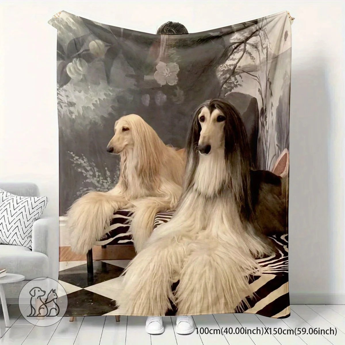 A soft, warm fleece throw blanket featuring a detailed retro artistic print of two long-haired Afghan Hound dogs against a vintage dark floral background, shown draped on a couch and laid over a bed in a home setting.