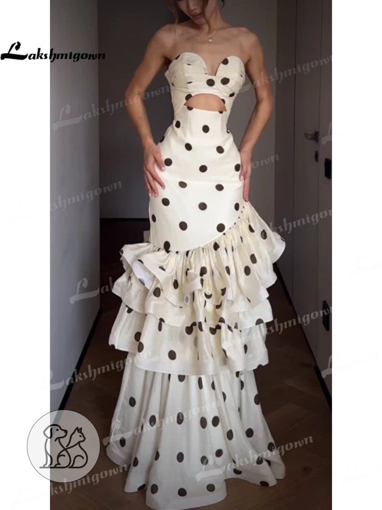 An elegant white mermaid evening gown featuring large black polka dots, a strapless sweetheart neckline with a modern front cut-out, and a dramatic tiered ruffled lower skirt shown from the front and back angles.