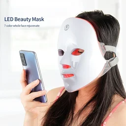 Woman using wireless LED beauty mask at home for facial skin tightening treatment