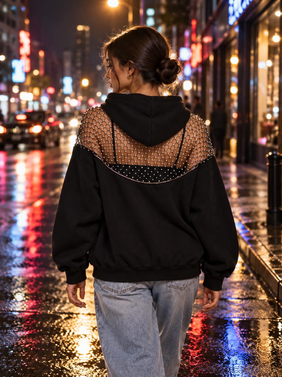 Woman walking away down a rain-wet city street at night in the black hoodie