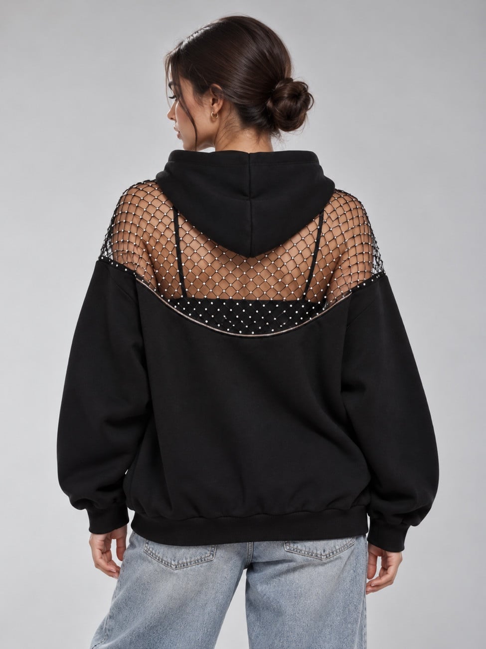 A woman seen from behind wearing the black Halo Mesh Hoodie; the rhinestone fishnet yoke shows over her shoulders