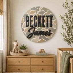 May include: A circular wall sign featuring a camouflage pattern in shades of tan, olive green, and cream. The name Beckett is displayed in large, black, sans-serif capital letters, with the name James in a black, cursive script font below.
