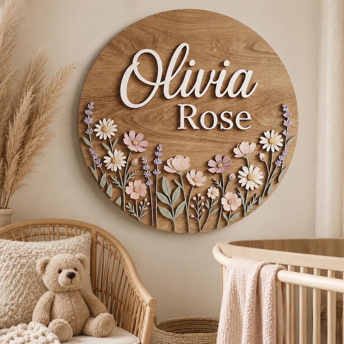 May include: A circular wooden wall sign featuring the name Olivia Rose in white 3D lettering. The lower portion is decorated with layered, cut-out floral elements including daisies, cosmos, and lavender sprigs in shades of pink, white, and green.