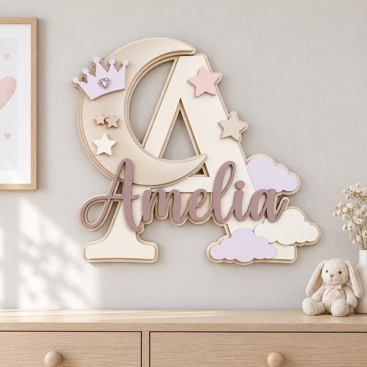 May include: A large, layered wooden wall decoration featuring the letter A, a crescent moon, and the name Amelia in cursive script. The design includes a light purple crown with a faux diamond, several stars in shades of pink and beige, and light purple and cream-colored clouds. The color palette consists of soft pastels, including cream, beige, dusty rose, and light purple.