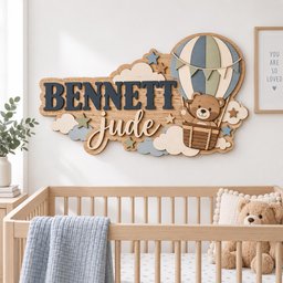 May include: A wooden wall sign featuring the name BENNETT Jude in dark blue and white lettering. The design includes a hot air balloon with a brown teddy bear in the basket, surrounded by light blue, white, and green clouds and stars.