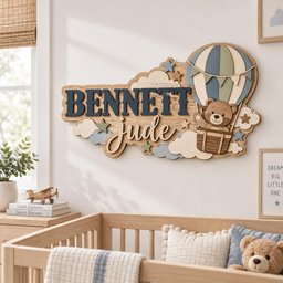 May include: A wooden wall sign featuring the name BENNETT in dark blue block letters and the name Jude in white script. The design includes a layered hot air balloon with a brown teddy bear in the basket, surrounded by clouds and small stars.