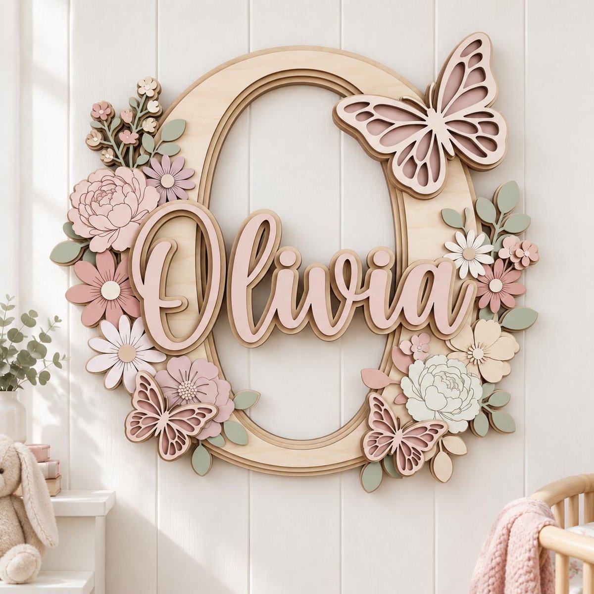May include: A layered wooden wall sign featuring a large letter O with the name Olivia in script lettering. The design is decorated with light pink and sage green wooden flowers and three butterflies in shades of pink and cream.