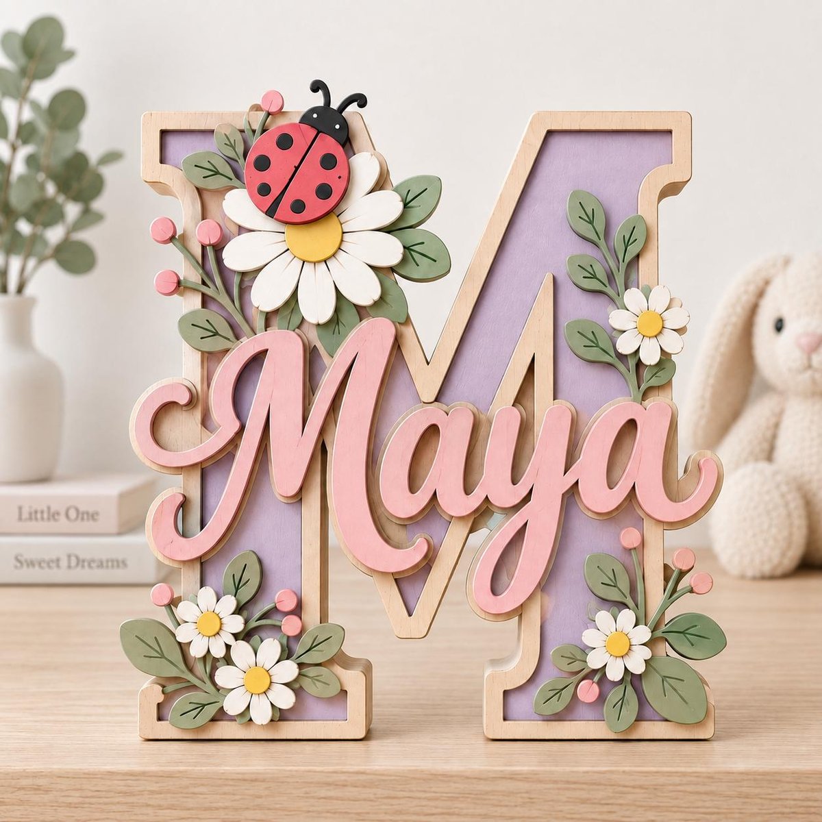 May include: A large wooden letter M with a light purple center and a light pink script name Maya attached to the front. The letter is decorated with white daisies, green leaves, small pink berries, and a red ladybug with black spots.