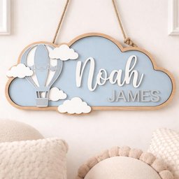 May include: A wooden cloud-shaped sign with a light blue background and a wooden frame. The sign features the name "Noah" in white script, the name "James" in gray block letters, a hot air balloon, and white cloud cutouts. The sign hangs from a rope.
