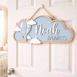 May include: A wooden cloud-shaped sign with a light blue background and a wooden border. It features a hot air balloon and the name "Noah James" in white and gray lettering. The sign is hanging on a white door.