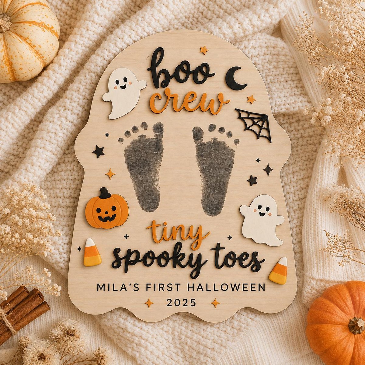 May include: A ghost-shaped wooden plaque featuring the text "boo crew" and "tiny spooky toes" with "MILA'S FIRST HALLOWEEN 2025" printed below. The plaque includes two black baby footprints, two white ghost cutouts, a pumpkin, and candy corn.