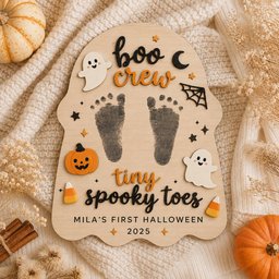May include: A ghost-shaped wooden plaque featuring the text "boo crew" and "tiny spooky toes" with "MILA'S FIRST HALLOWEEN 2025" printed below. The plaque includes two black baby footprints, two white ghost cutouts, a pumpkin, and candy corn.