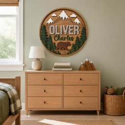 May include: A circular wooden wall sign featuring a layered mountain landscape with white peaks, green pine trees, and a brown bear silhouette. The text "OLIVER" is in white block letters, and "Charles" is in dark green script below the name.