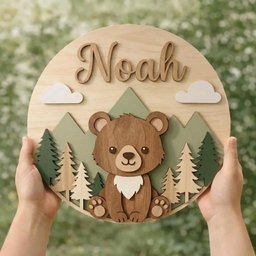 May include: Wooden round wall decor featuring a bear, mountains, trees, and clouds. The name "Noah" is displayed in cursive lettering. The bear is brown with a white chest. The mountains are green and the trees are light brown and green.
