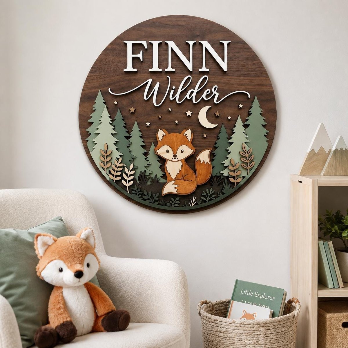 May include: A circular wooden wall sign featuring the name FINN Wilder in white lettering. The design includes a layered forest scene with green pine trees, a central orange and white fox, a crescent moon, and small stars on a dark wood background.
