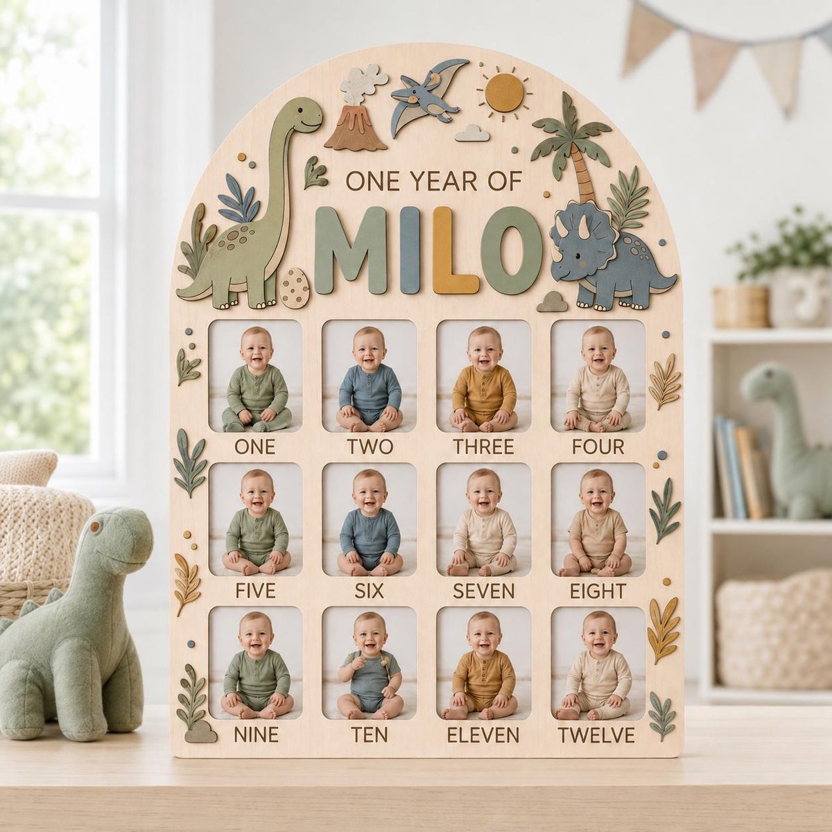 May include: A wooden arched photo display board titled ONE YEAR OF MILO, featuring dinosaur-themed decorations including a volcano, pterodactyl, and palm trees. It contains twelve rectangular slots for monthly baby photos labeled one through twelve.